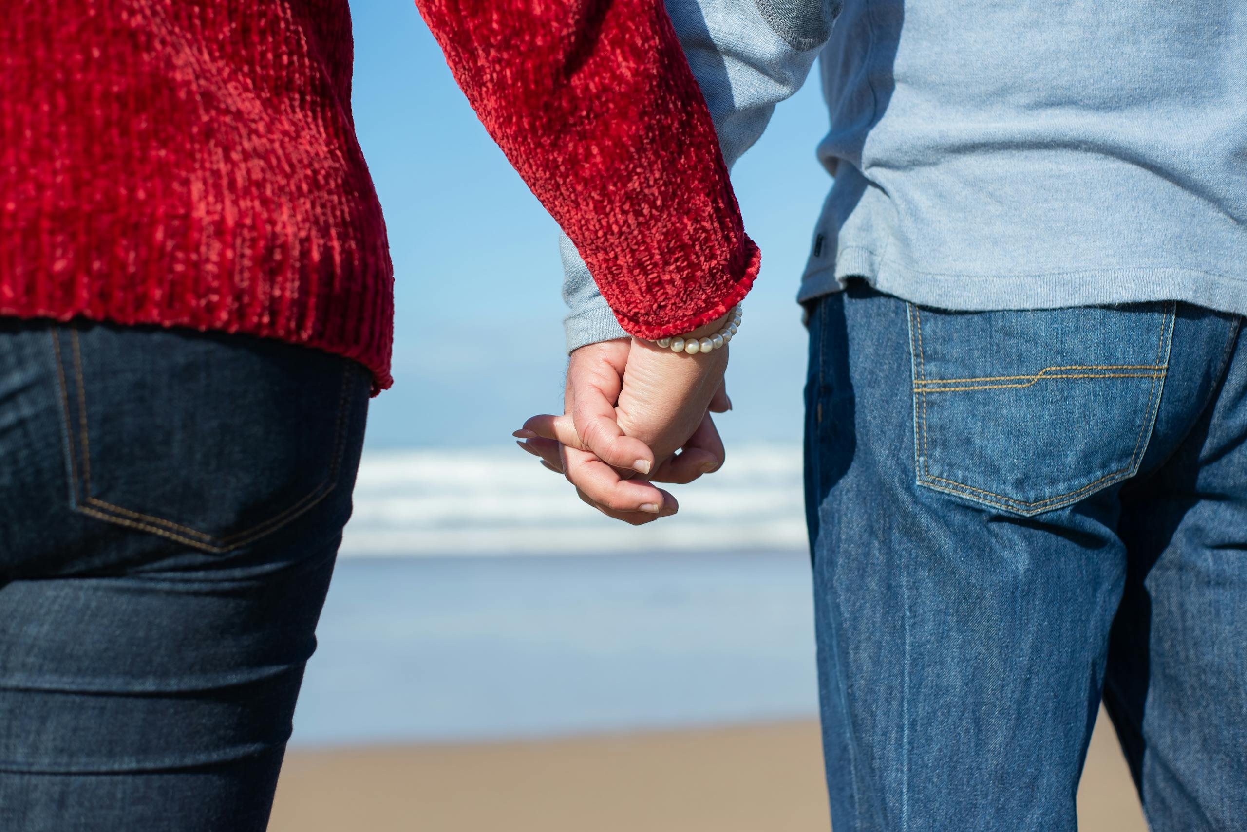 A close-up of a couple holding hands on a beach in Portugal, capturing intimacy.
